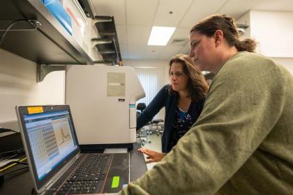 Two professors standing in a lab looking at a computer